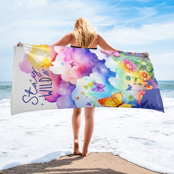 Chica con toalla multicolor Stay Wild en bruma de la playa. La toalla con nubes de colores, mariposas y flores.