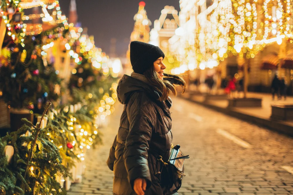 Una chica en la calle, en un mercadillo de Navidad, rodeada de luces y feliz.