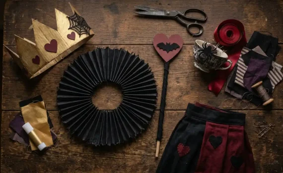 Corona dorada con corazones granate, gorguera negra plisada, cetro con corazón y murciélago y falda negra y granate para un disfraz de Reina de Corazones de Halloween